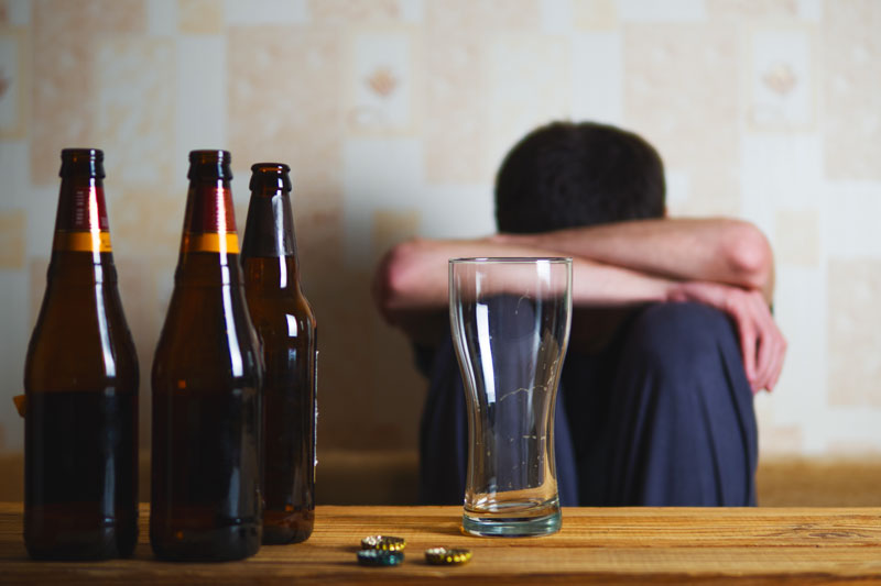 man with head on knees sad empty alcohol bottles - alcoholism treatment in Kansas