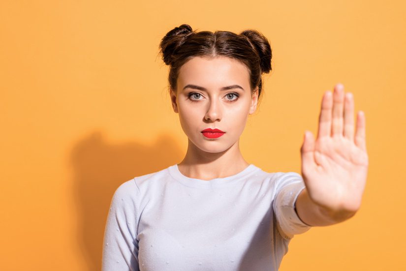 pretty young woman on yellow background holding hand up in 'stop' gesture - excuses
