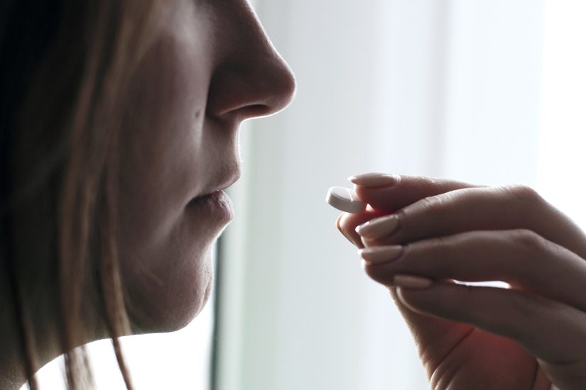 closeup of woman taking a white pill - chronic pain