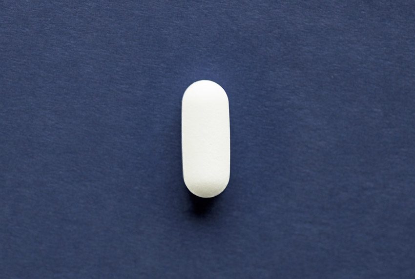 Xanax Misuse, white oblong tablet on dark blue paper background - Xanax