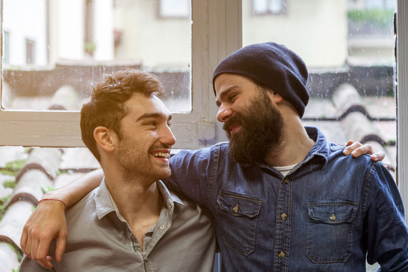 two male friends smiling - one has his arm around the other's shoulders - friend