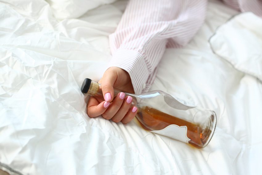cropped shot of woman's arm in bed holding bottle of alcohol - blackouts