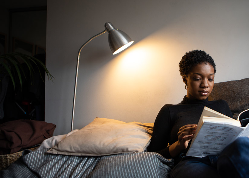 gorgeous Black woman with short hair reading a book by lamp light in her bedroom - mindfulness