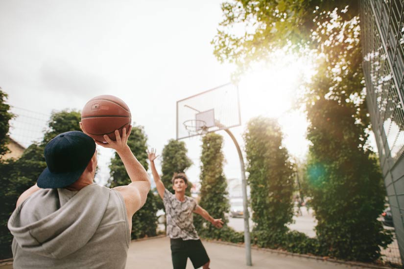 two Caucasian young men playing a game of pick up basketball outside - exercise routine